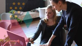 two women in business attire looking at a computer screen